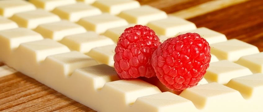 Two raspberries on top of a piece of white chocolate.