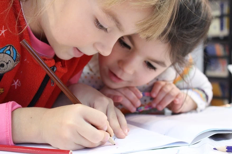 Two young girls writing in a school notebook.
