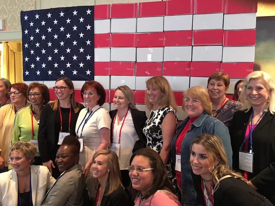 A charitable group of women posing in front of an American flag.