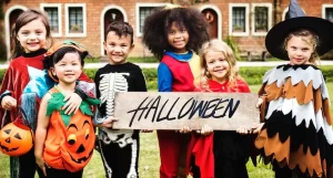 A group of children in Halloween costumes, having a blast while holding a sign.