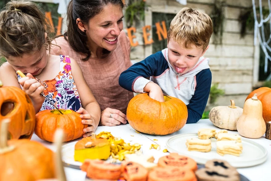 A woman and children are decorating pumpkins for Thanksgiving at a table.