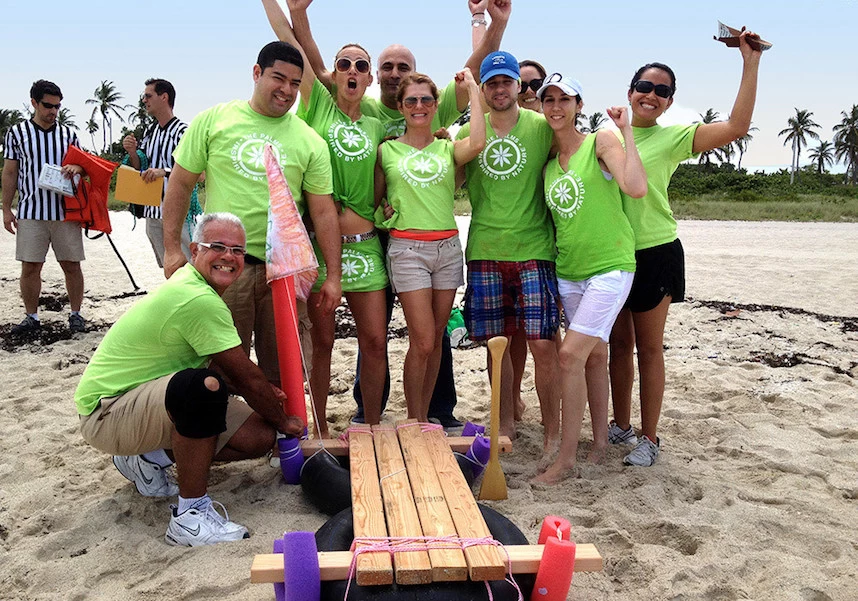 A team of people posing with a wooden boat on the beach as part of their team building activity.