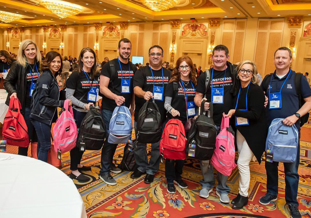 A group of people posing with backpacks in a conference room.