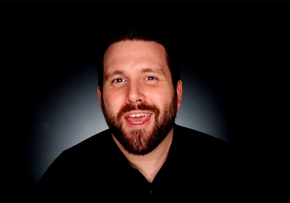 A man with a beard is smiling in front of a black background.