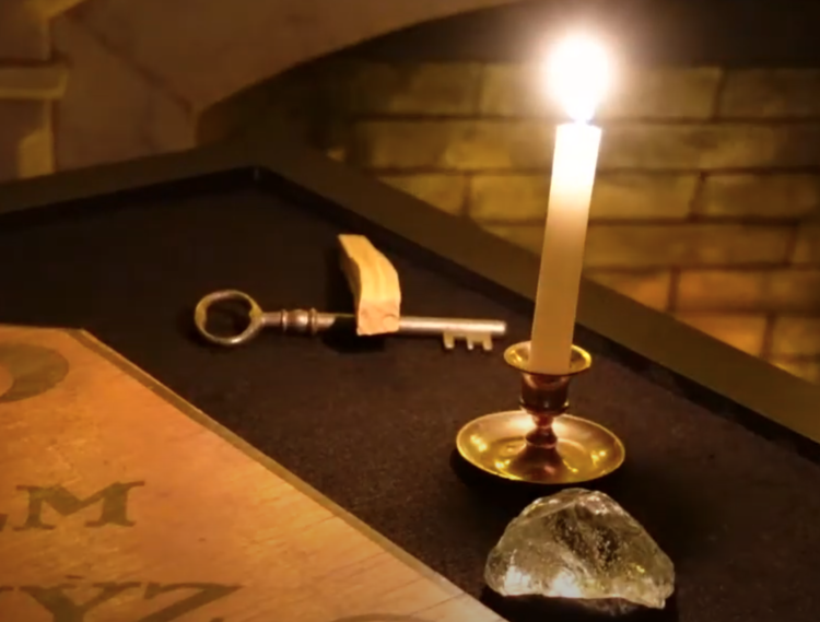 A candle sits on a table next to a book and a key.