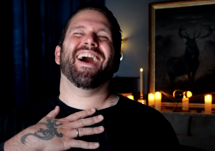 A man with a beard and tattoos is laughing in front of candles.