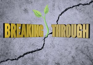 The word breaking through is written on a crack in a concrete wall.