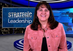 A woman standing in front of a television screen with the words strategic leadership.