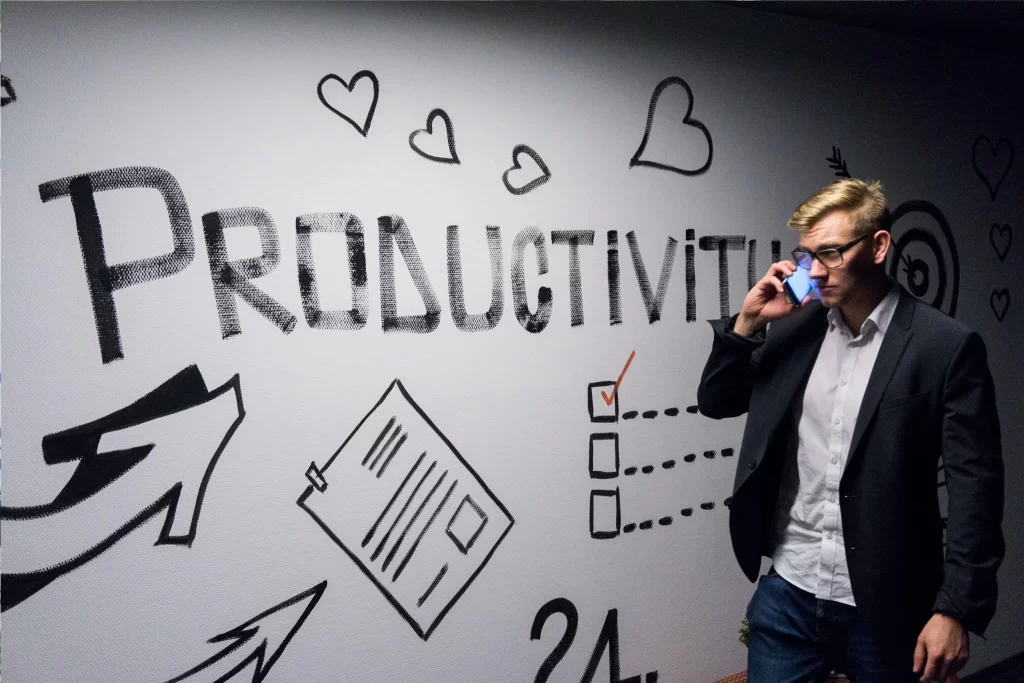 A businessman making new employees productive, talking on the phone in front of a wall with the word productivity written on it.