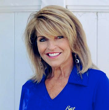 A woman in a blue shirt smiling in front of a white wall.