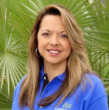 A woman in a blue shirt standing in front of palm trees.