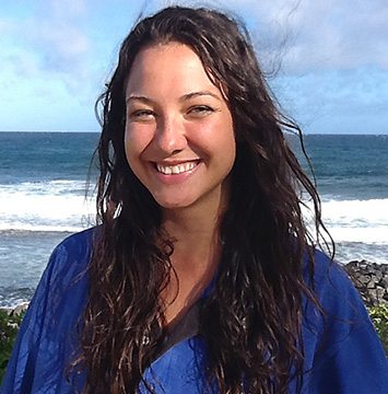 A woman in a blue robe smiling in front of the ocean.