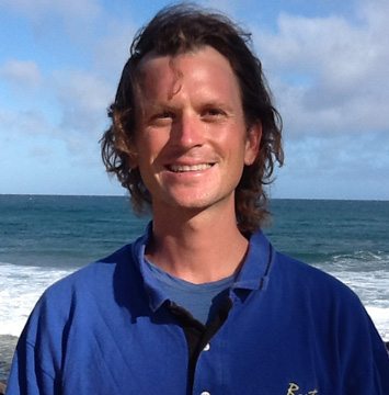 A man in a blue shirt standing in front of the ocean.