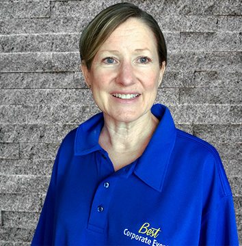 A woman in a blue shirt standing in front of a brick wall.