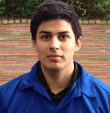 A young man in a blue shirt standing in front of a brick wall.