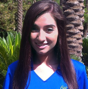 A young woman in a blue shirt standing in front of palm trees.