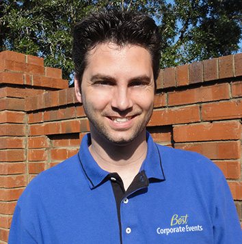 A man in a blue shirt standing in front of a brick wall.