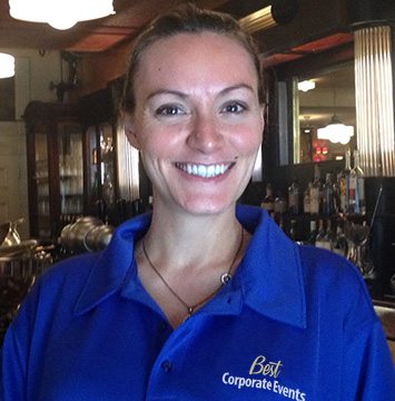 A woman in a blue shirt standing in front of a bar.