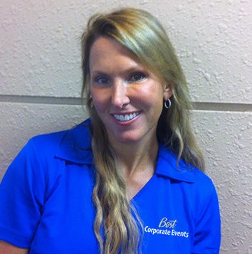 A woman in a blue shirt smiling in front of a wall.