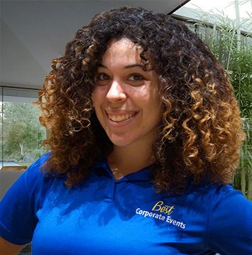 A woman with curly hair smiling in a blue shirt.