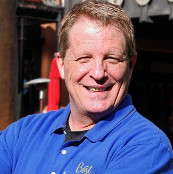 A man in a blue shirt smiling in front of a restaurant.