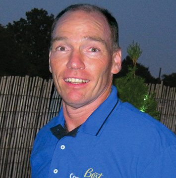 A man in a blue shirt standing in front of a fence.