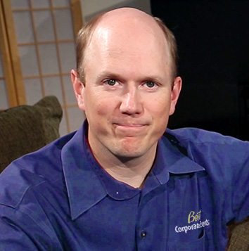 A bald man in a blue shirt sitting on a couch.