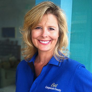 A woman in a blue shirt smiling in front of a window.