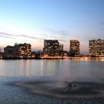 A city at dusk with a fountain in the middle of a lake.