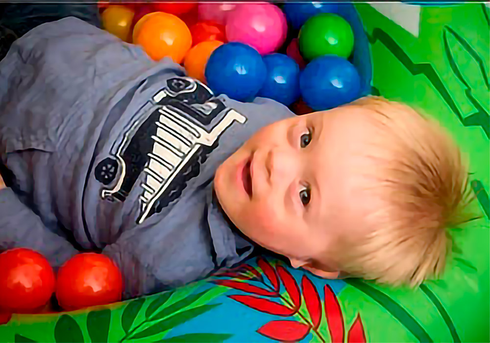 A young boy laying in a colorful ball pit.