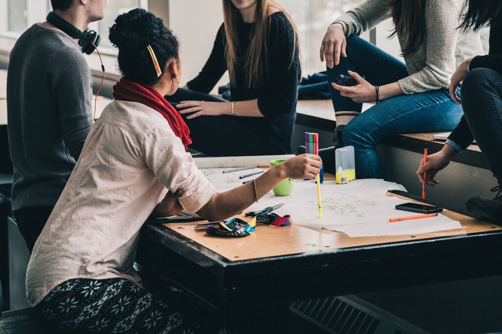 A group of people gathered around a table with papers and markers, engaged in conversation, strategizing how to measure team building success.