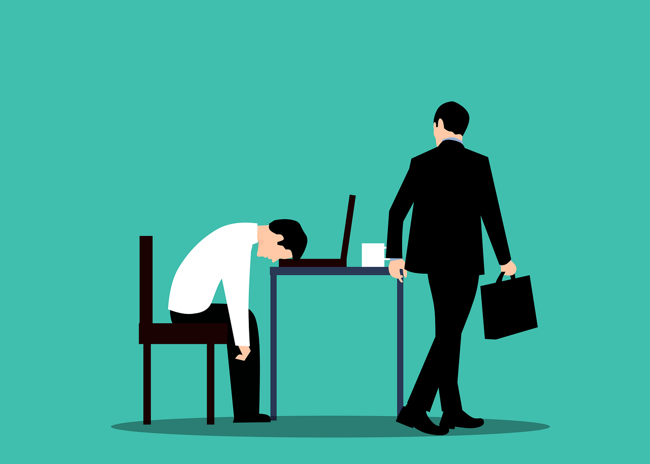 A businessman is sitting at a desk with his head down.