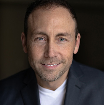 A man in a suit and white shirt is smiling.