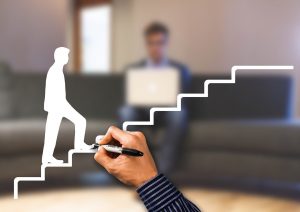 Hand drawing a staircase leading to a man with a laptop, symbolizing progress or career advancement, with a blurred background.