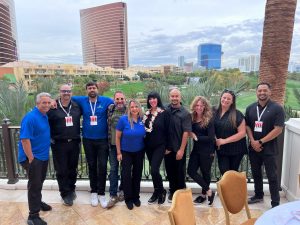 A group of ten people, fresh from a conference, posing together on an outdoor terrace with a cityscape and green landscape in the background, epitomizing team building at its finest.
