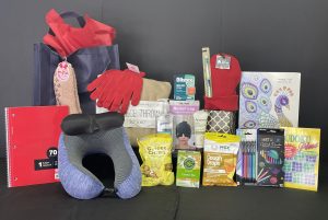 Assortment of wellness and comfort items in our cancer care packs, including a neck pillow, ginger chews, a coloring book, a notebook, gloves, throat spray, cough drops, a sleep mask, a pen set, and lip balm.