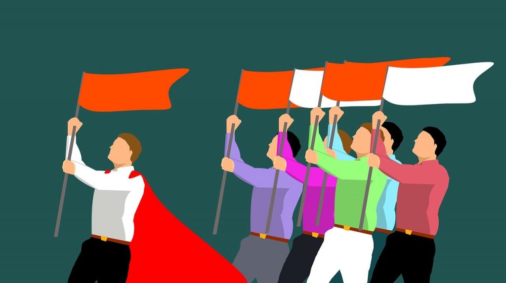 Illustration of six people marching with red and white flags, led by a person wearing a red cape and waving a red flag, symbolizing the contrast between leadership vs management.