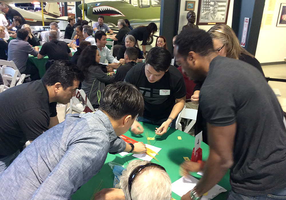 Group of people at a table engaged in a team-building activity inside a room with aircraft displays.