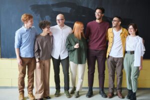 Seven people, dressed casually and smiling brightly, stand in front of a chalkboard—an inspiring snapshot of collaboration that hints at their shared mission to understand how to improve workplace culture.