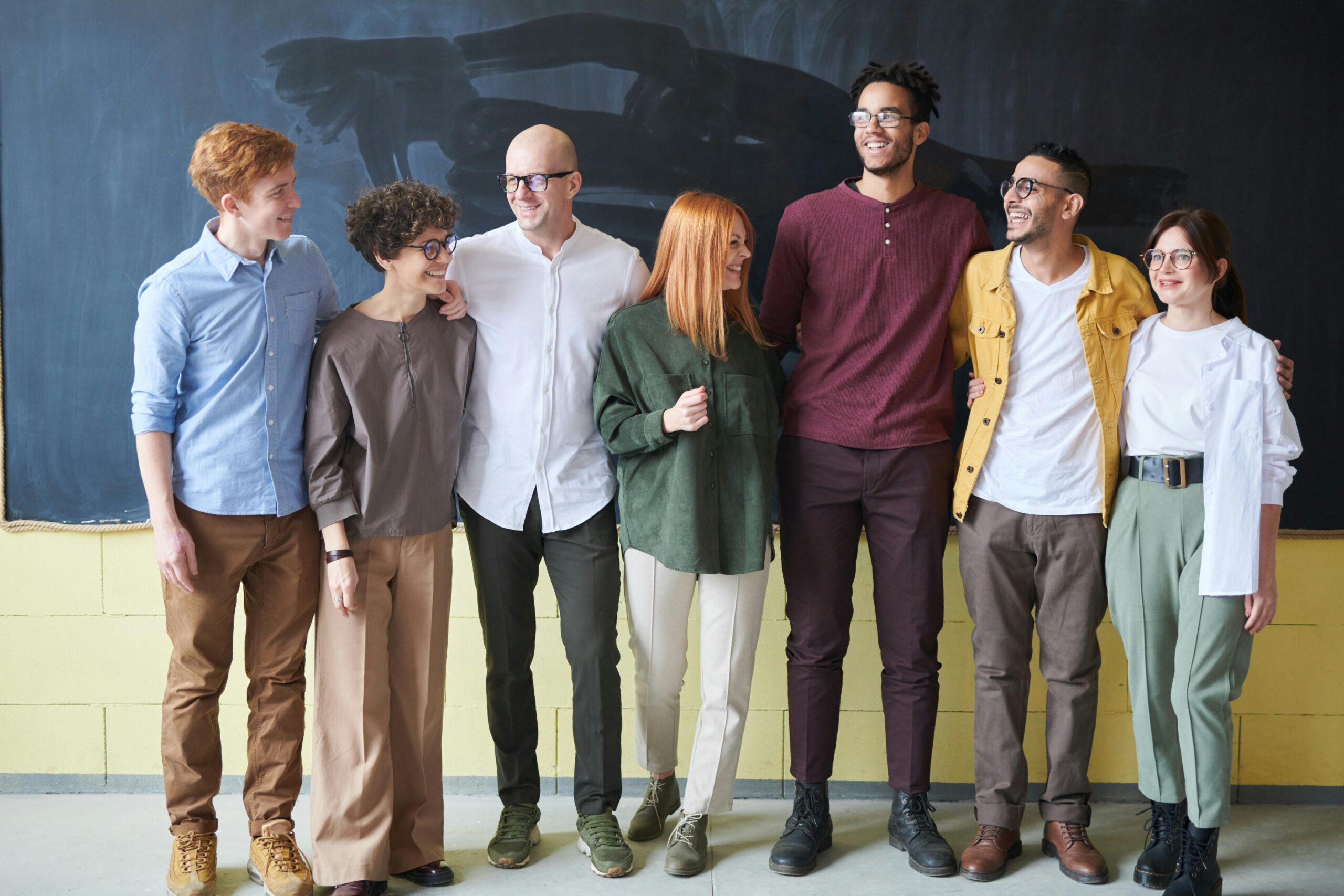 Seven people, dressed casually and smiling brightly, stand in front of a chalkboard&mdash;an inspiring snapshot of collaboration that hints at their shared mission to understand how to improve workplace culture.