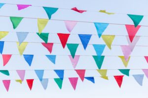 Colorful triangular pennant flags hang on several strings against a clear blue sky.