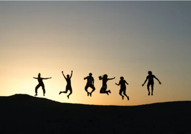 Silhouette of a team leaping joyfully in the air against a sunset sky on a hilltop, embodying the spirit of team building and boosting employee morale.