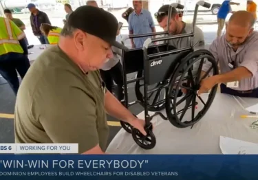 A man from Dominion Energy is working on a wheelchair in front of a group of people while showcasing their commitment towards building inclusive mobility solutions.