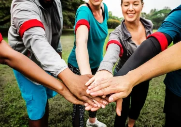 A group of people participating in team building exercises, putting their hands together in a circle.