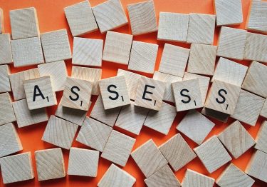 Scrabble tiles on a wooden surface spell out the word "ASSESS" amid scattered blank tiles, highlighting the importance of a leadership potential assessment.