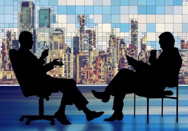 Two silhouettes of business people actively listening to each other in front of a city skyline.