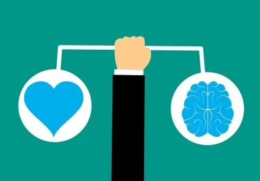 A hand holding a scale with a heart and a brain on it, representing the concept of emotional intelligence.