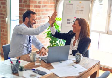 Two business people giving each other high fives in an office.