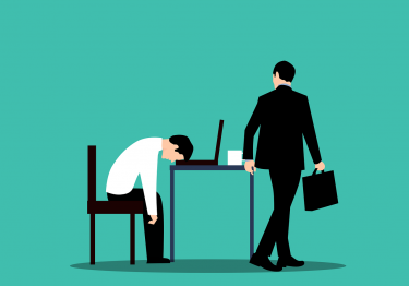 A businessman is sitting at a desk with his head down.
