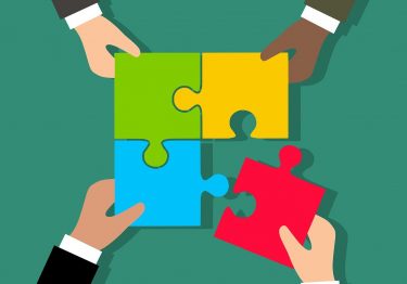 A group of corporate hands holding a puzzle piece together in a show of event partnerships.